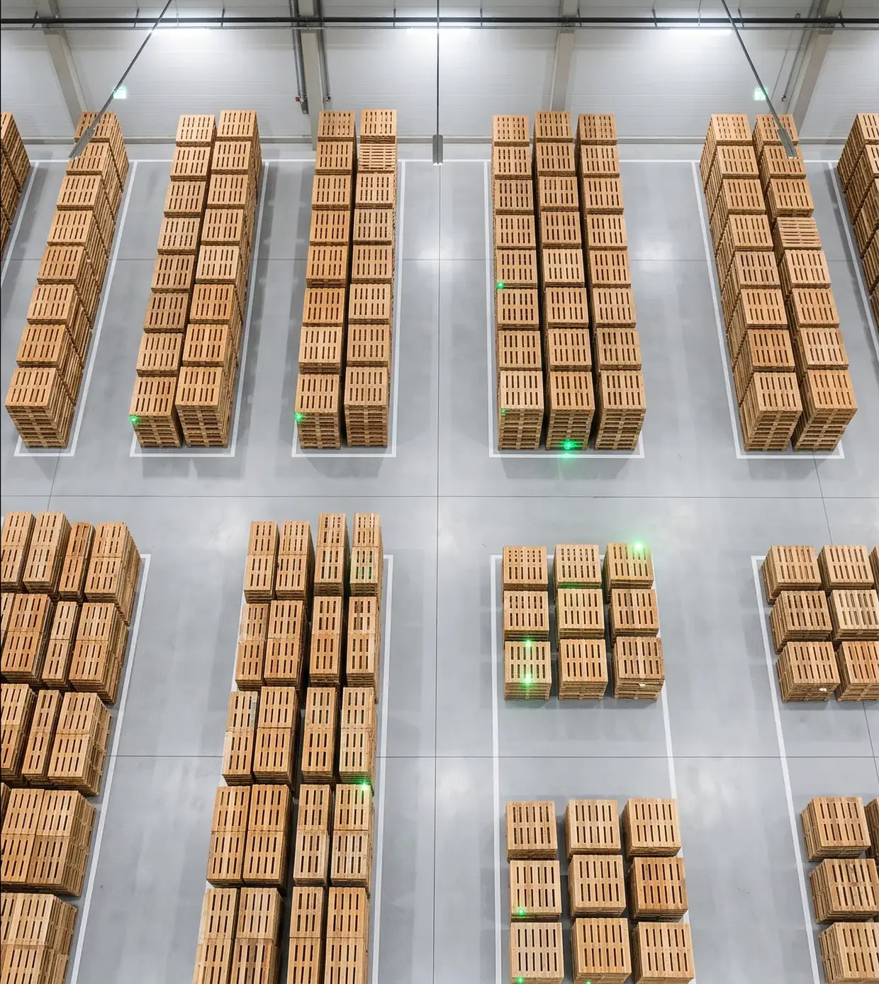 Galpão organizado: pilhas de pallets alinhadas em áreas demarcadas, cada uma com um ponto de luz verde de rastreio