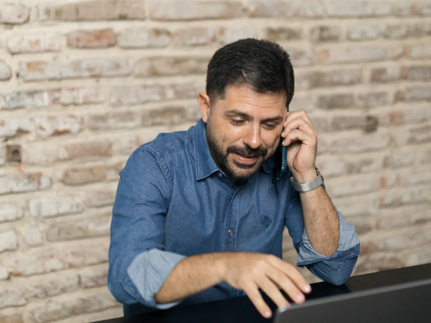 Tiago Asfora ao telefone, na mesa de trabalho, com notebook e caderno